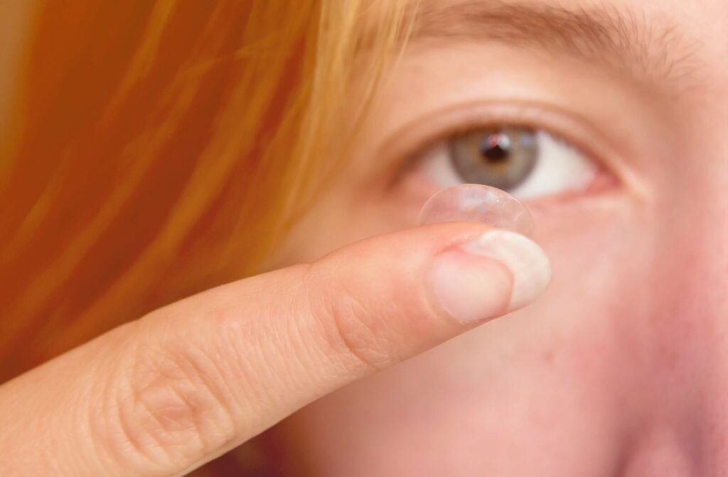 A woman pausing before she inserts a contact lens into her right eye with her right index finger.