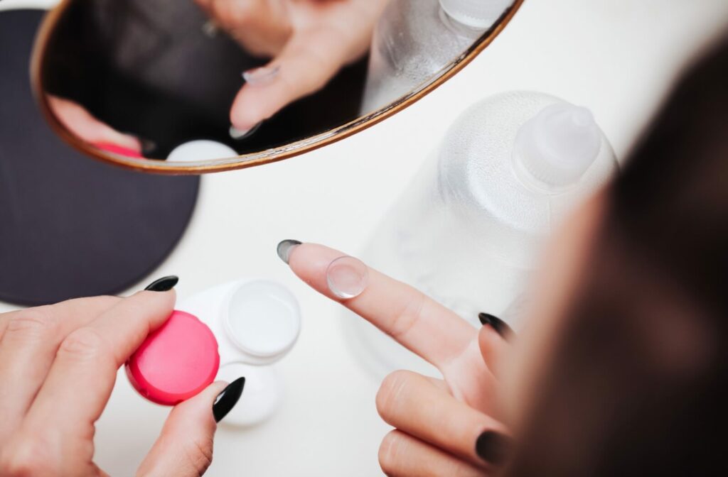 A person cleans their contact lens in front of a mirror before storing it in the case overnight.