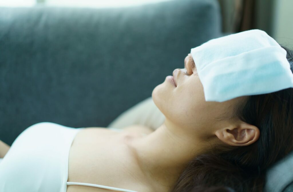 A woman lies down on a couch, a warm compress covering both eyes as a way to relieve dry eye symptoms