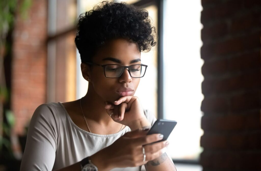 A person wearing glasses texting on their cellphone