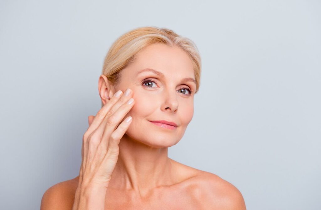 Youthful older blonde woman with smooth skin smiling and touching the side of her cheek.
