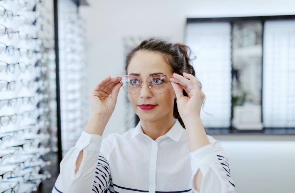 A young adult tries on new eyeglasses frames in their eye doctor's office showroom.