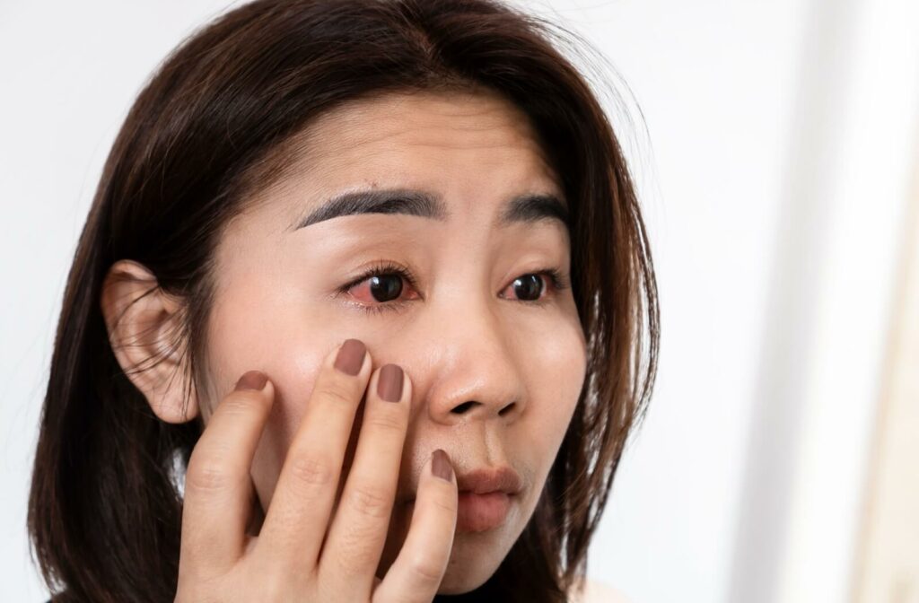 A person looks in the mirror with red, irritated eyes, gently touching their lower eyelid.
