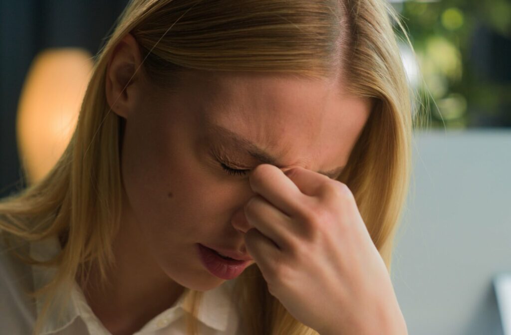 Close-up of a woman pressing the bridge of her nose with her eyes closed, appearing to experience eye strain or discomfort.