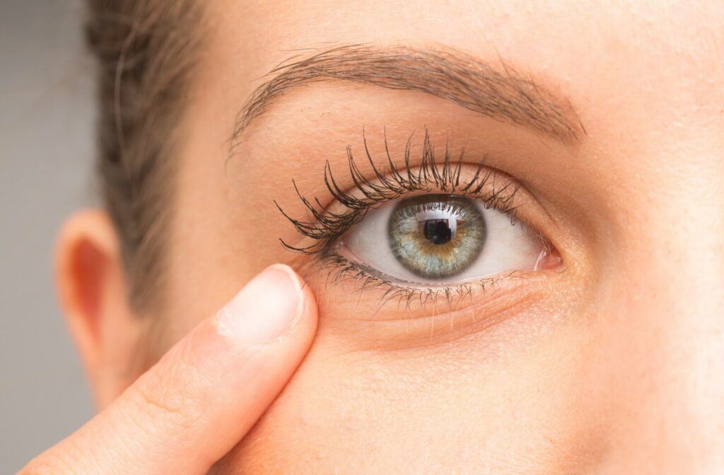 A close-up of an eye with a person gently touching the skin beneath the lower eyelid, showing long eyelashes and a detailed view of the iris.
